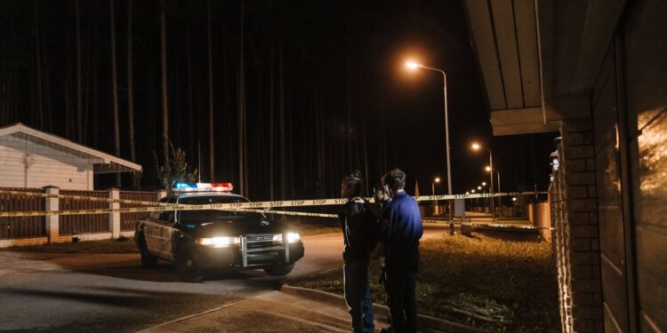 Gece vakti sokakta polis ekipleri ve güvenlik şeridi önünde duran şüpheli