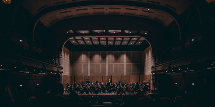 Devasa tarihi konser salonunun sahnesinde performans sergileyen geniş senfoni orkestrası.