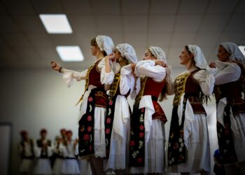 Geleneksel kıyafetler giymiş kadınlar el ele tutuşup halay çekiyor.