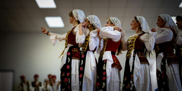 Geleneksel kıyafetler giymiş kadınlar el ele tutuşup halay çekiyor.