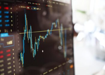 Bilgisayar ekranında mavi ve sarı renkli borsa grafik çizgileri görünmektedir.