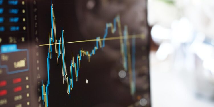 Bilgisayar ekranında mavi ve sarı renkli borsa grafik çizgileri görünmektedir.