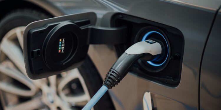 Gri renkli elektrikli bir otomobilin şarj istasyonundan kablo ile şarj edilişi.