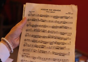 Elinde Türk sanat müziği notaları ve Hûzzam Saz Semâîsi yazan kağıt tutulan bir an.