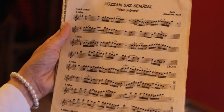 Elinde Türk sanat müziği notaları ve Hûzzam Saz Semâîsi yazan kağıt tutulan bir an.