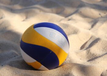 Kumsaldaki kumların üzerine bırakılmış mavi, sarı ve beyaz renkli voleybol topu.