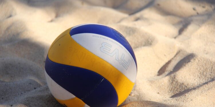Kumsaldaki kumların üzerine bırakılmış mavi, sarı ve beyaz renkli voleybol topu.