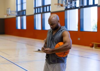Antrenörlük kıyafeti giymiş, elinde basketbol topu ve pano tutan koç.