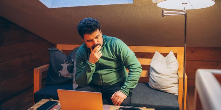 Yeşil kazaklı bir adam loş bir odada dizüstü bilgisayara bakıyor.