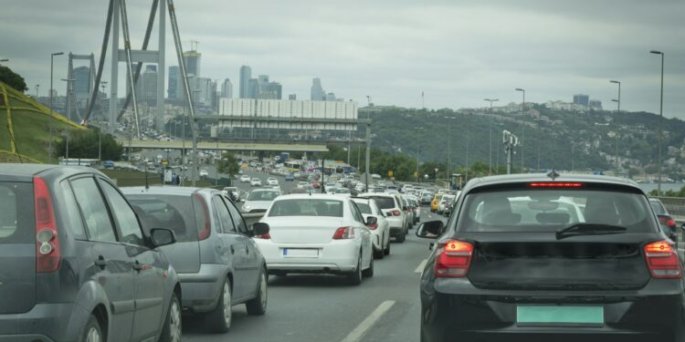İstanbul köprüsü üzerinde yoğun trafikte sıkışmış araçlar ve arka planda şehir silüeti.