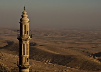 Tarihi bir cami minaresi ve arkasında engin dağlık bozkır manzarası.
