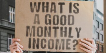 Üzerinde 'What is a good monthly income?' yazan karton tabela tutan bir kişi.