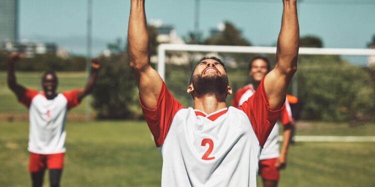 Kollarını havaya kaldırarak sevinç çığlığı atan sporcu ve arka planda takım arkadaşları.