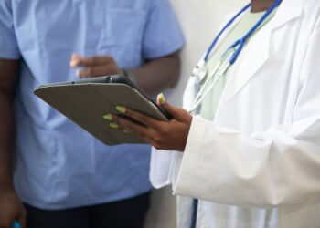 Sağlık çalışanı ellerinde koruyucu kılıf içinde tablet bilgisayar tutuyor.