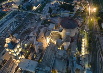 Gece vakti ışıklandırılmış modern bir endüstriyel fabrika tesisinin havadan görünümü.