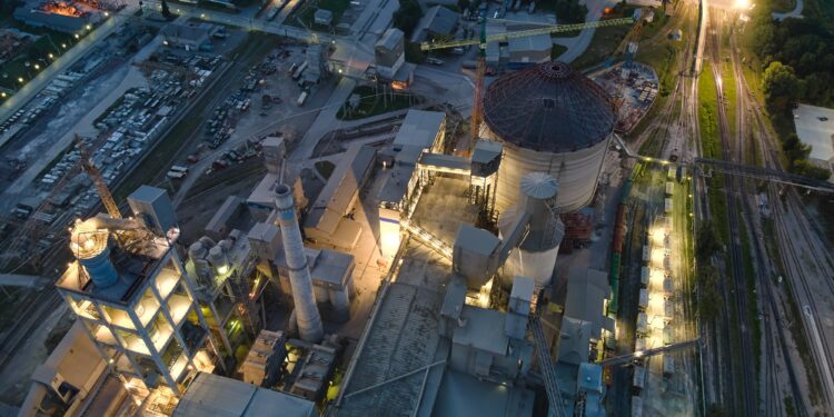 Gece vakti ışıklandırılmış modern bir endüstriyel fabrika tesisinin havadan görünümü.