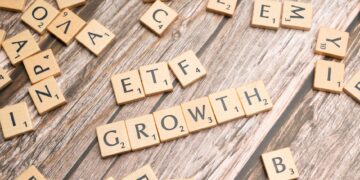 Ahşap masa üzerinde ETF ve GROWTH yazan Scrabble harfleri ve etraftaki harfler.