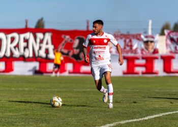 Forma giymiş bir futbolcu yeşil sahada top sürerken görülüyor.