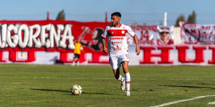 Forma giymiş bir futbolcu yeşil sahada top sürerken görülüyor.