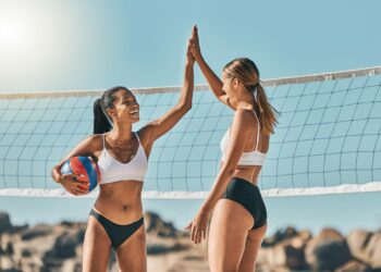 Plaj voleybolu oynayan iki kadın oyuncu file önünde neşeyle kutlama yapıyor.