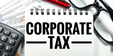 Üzerinde 'CORPORATE TAX' yazan not defteri, hesap makinesi ve gözlük.