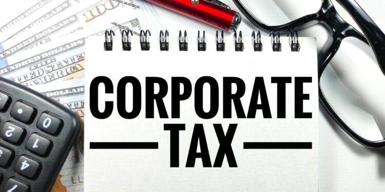 Üzerinde 'CORPORATE TAX' yazan not defteri, hesap makinesi ve gözlük.