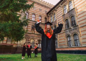 Mezuniyet cübbesi giymiş, ellerinde diplomalarla mutlu şekilde tezahürat yapan öğrenciler.