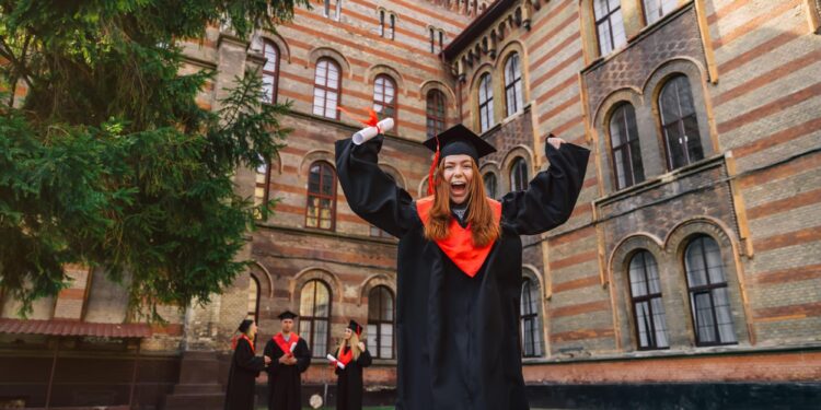 Mezuniyet cübbesi giymiş, ellerinde diplomalarla mutlu şekilde tezahürat yapan öğrenciler.